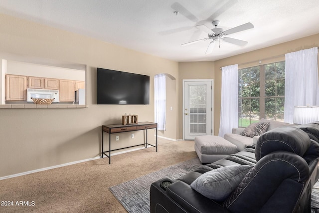 living area with light carpet, baseboards, arched walkways, and ceiling fan