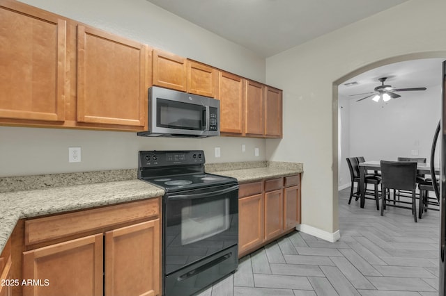 kitchen with arched walkways, a ceiling fan, stainless steel microwave, light stone countertops, and black electric range