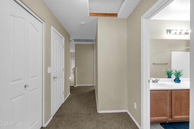 hallway featuring baseboards, visible vents, a sink, and carpet flooring