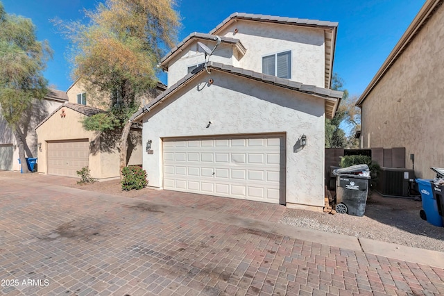 traditional-style home with a garage, a tile roof, decorative driveway, and stucco siding