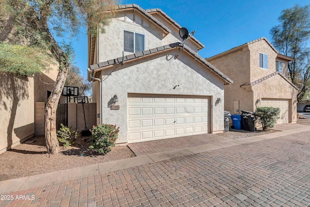 view of front of property featuring a garage, fence, decorative driveway, and stucco siding