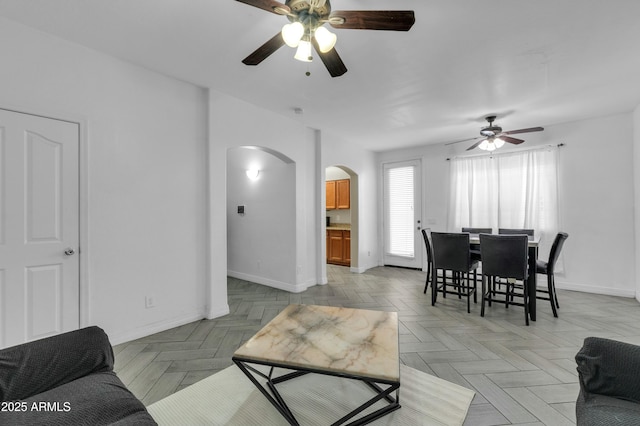 living area with a ceiling fan, arched walkways, and baseboards