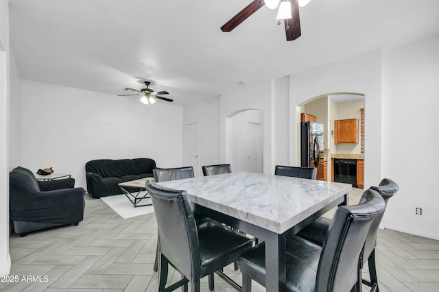 dining room with ceiling fan, arched walkways, and baseboards