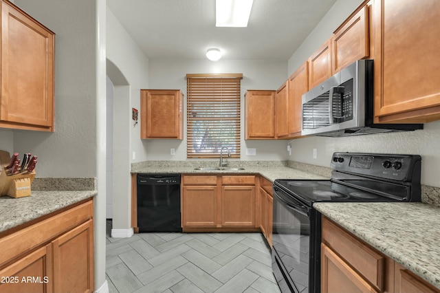 kitchen featuring black appliances, brown cabinets, a sink, and light stone countertops