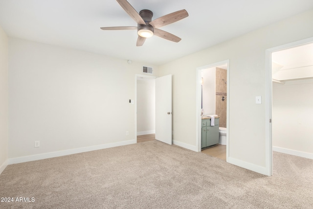 unfurnished bedroom featuring ensuite bathroom, ceiling fan, a walk in closet, light colored carpet, and a closet