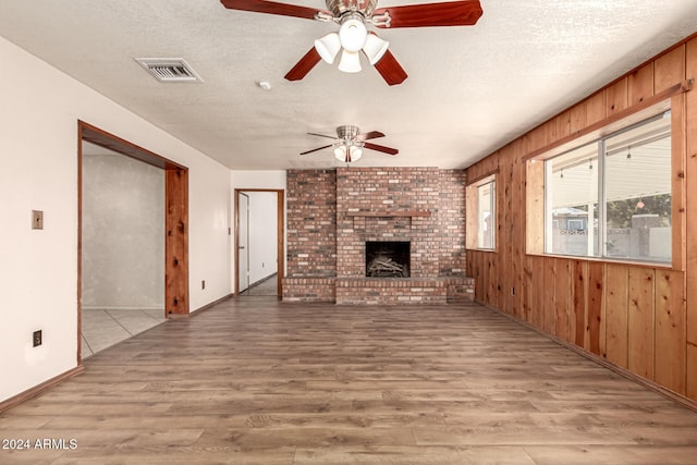 unfurnished living room featuring a brick fireplace, light hardwood / wood-style flooring, and wooden walls