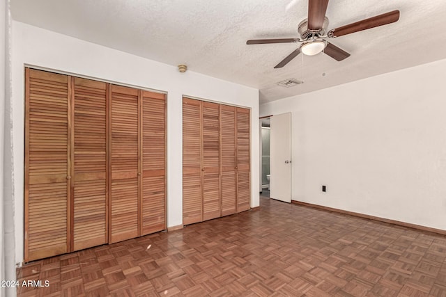 unfurnished bedroom featuring ceiling fan, dark parquet floors, a textured ceiling, and two closets