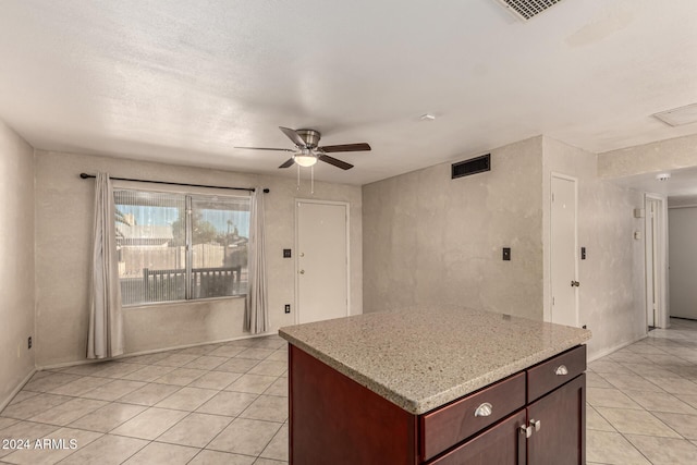 kitchen with ceiling fan, a center island, light stone counters, and light tile patterned floors