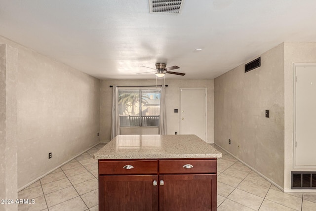 kitchen with ceiling fan, a kitchen island, light stone countertops, and light tile patterned floors