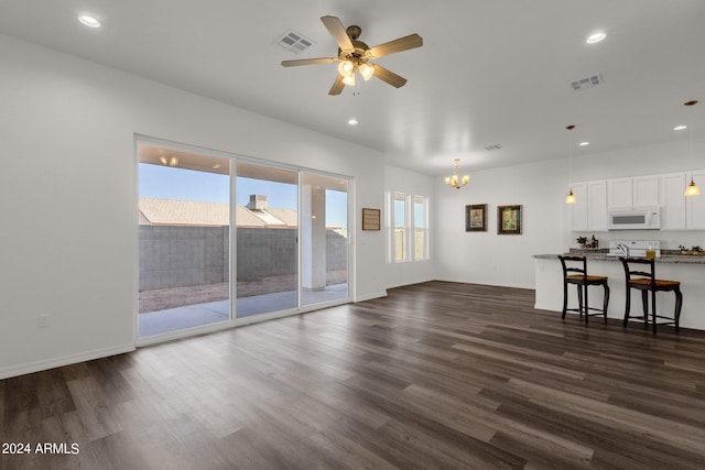 unfurnished living room featuring ceiling fan with notable chandelier and dark hardwood / wood-style floors