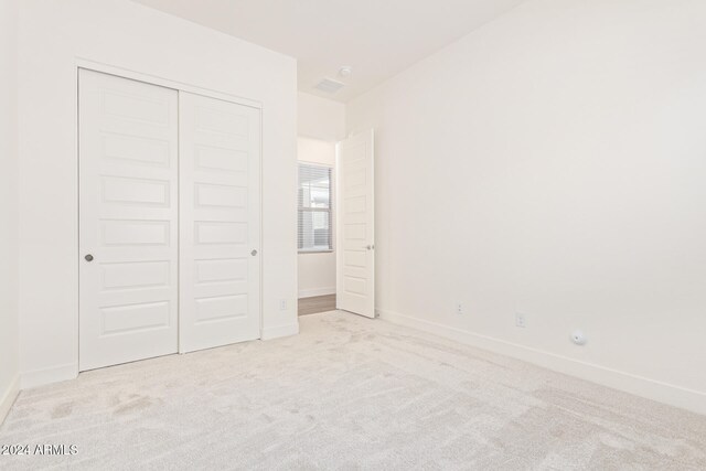 unfurnished bedroom with light colored carpet and a closet