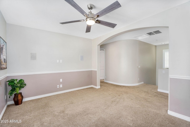carpeted empty room featuring a ceiling fan, visible vents, arched walkways, and baseboards