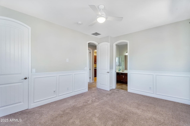 interior space featuring visible vents, light carpet, ensuite bathroom, arched walkways, and ceiling fan