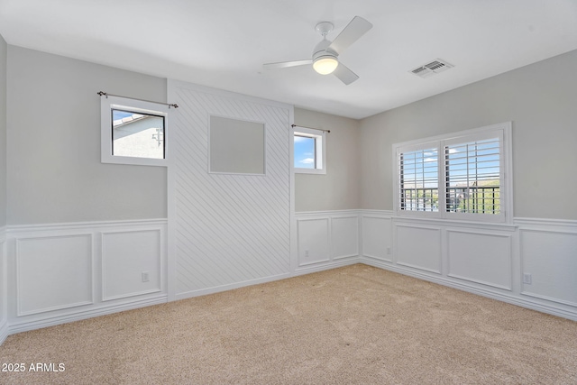 empty room featuring a wainscoted wall, visible vents, and light carpet