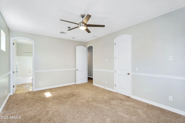 unfurnished bedroom with visible vents, connected bathroom, arched walkways, baseboards, and light colored carpet