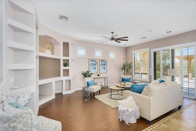 living room with visible vents, built in features, wood finished floors, baseboards, and ceiling fan