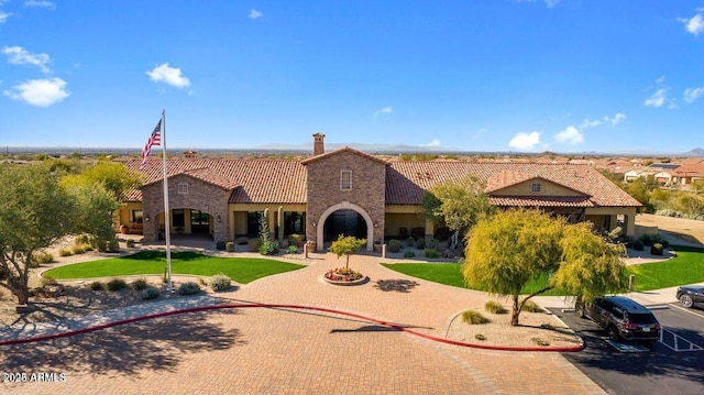 mediterranean / spanish house featuring a chimney, stucco siding, a tile roof, and a front yard