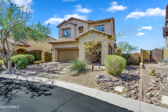 mediterranean / spanish-style house with stucco siding, driveway, a gate, an attached garage, and a tiled roof