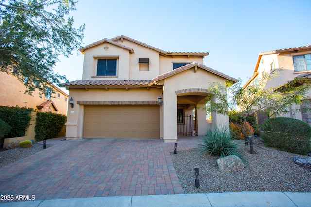 mediterranean / spanish home featuring a tiled roof, decorative driveway, a garage, and stucco siding