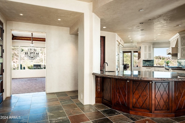 kitchen featuring dark colored carpet, an inviting chandelier, decorative backsplash, sink, and decorative light fixtures