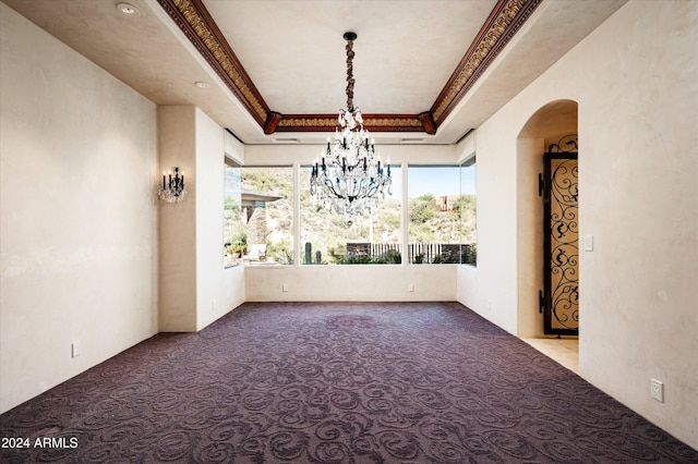 carpeted spare room featuring a raised ceiling, an inviting chandelier, and ornamental molding