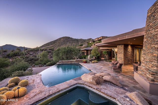 pool at dusk with a mountain view, an in ground hot tub, and a patio area