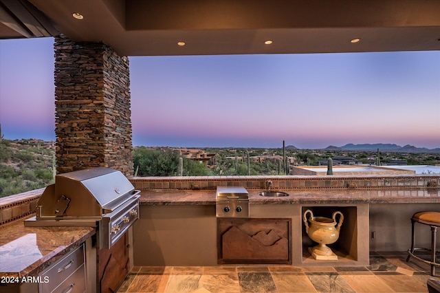 patio terrace at dusk with a mountain view, sink, an outdoor kitchen, and a grill