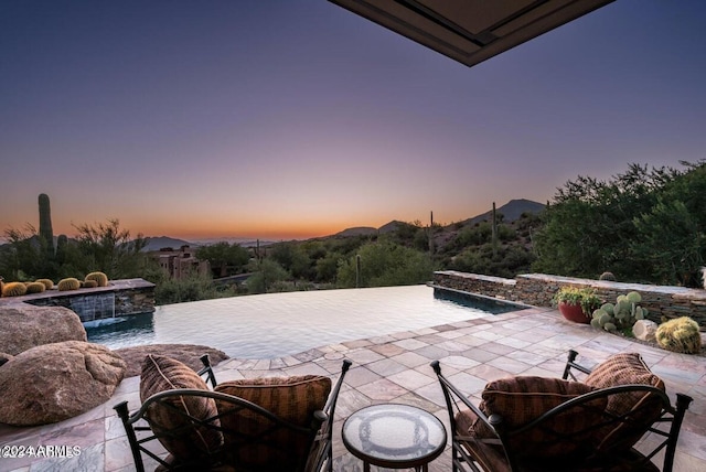 pool at dusk with a mountain view, pool water feature, and a patio area