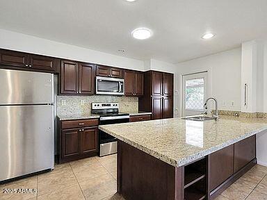 kitchen featuring dark brown cabinetry, appliances with stainless steel finishes, a sink, light tile patterned floors, and a peninsula