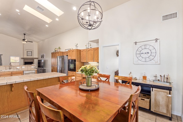 tiled dining room featuring ceiling fan with notable chandelier, high vaulted ceiling, sink, and a skylight