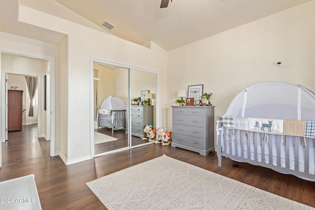 bedroom featuring ceiling fan, a crib, lofted ceiling, dark wood-type flooring, and a closet