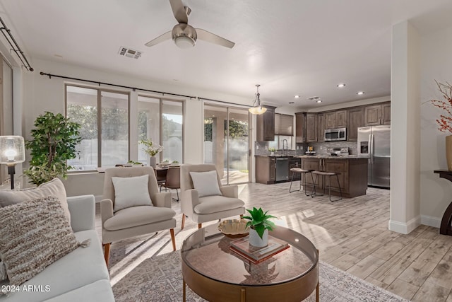 living room featuring ceiling fan, sink, and light wood-type flooring