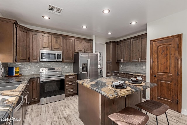 kitchen with appliances with stainless steel finishes, tasteful backsplash, dark stone counters, a center island, and light hardwood / wood-style floors