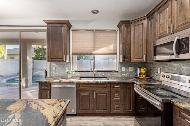 kitchen with a healthy amount of sunlight, sink, appliances with stainless steel finishes, and dark stone counters