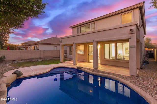 back house at dusk featuring a fenced in pool and a patio area