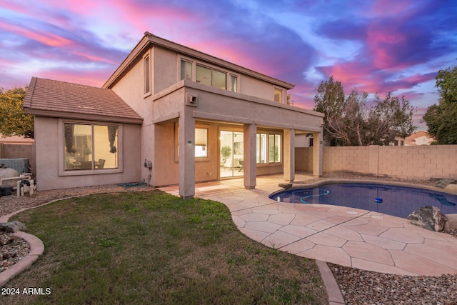 back house at dusk with a balcony, a yard, a fenced in pool, and a patio area