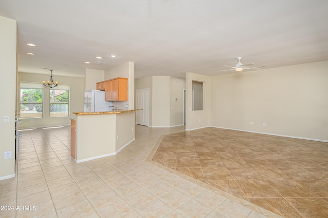 kitchen featuring light tile patterned floors, kitchen peninsula, white fridge, pendant lighting, and ceiling fan with notable chandelier