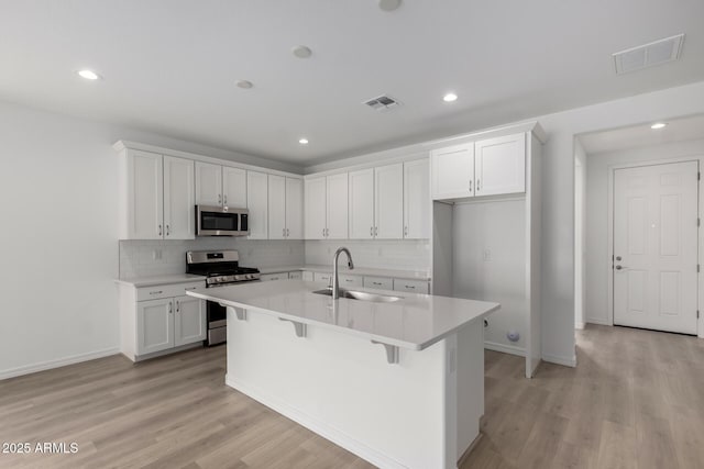 kitchen with sink, white cabinetry, stainless steel appliances, and an island with sink