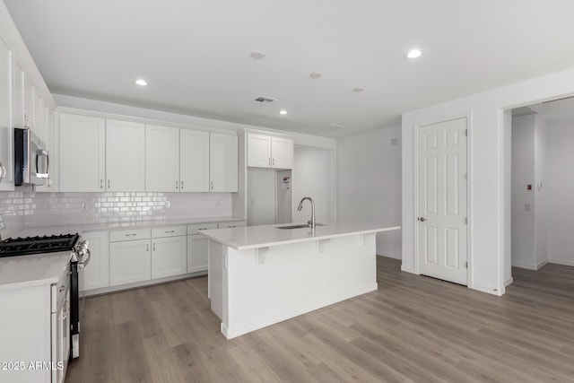 kitchen featuring tasteful backsplash, stainless steel appliances, sink, white cabinetry, and an island with sink