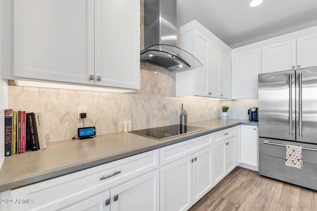 kitchen featuring stainless steel built in fridge, light wood-type flooring, white cabinetry, wall chimney range hood, and black electric cooktop