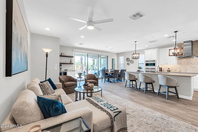 living room featuring ceiling fan with notable chandelier and light hardwood / wood-style floors