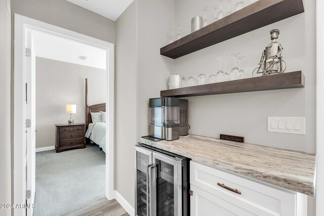 bar with light carpet, white cabinetry, beverage cooler, and light stone countertops