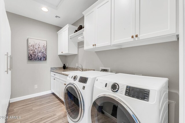 clothes washing area featuring washer and dryer, cabinets, sink, and light hardwood / wood-style floors