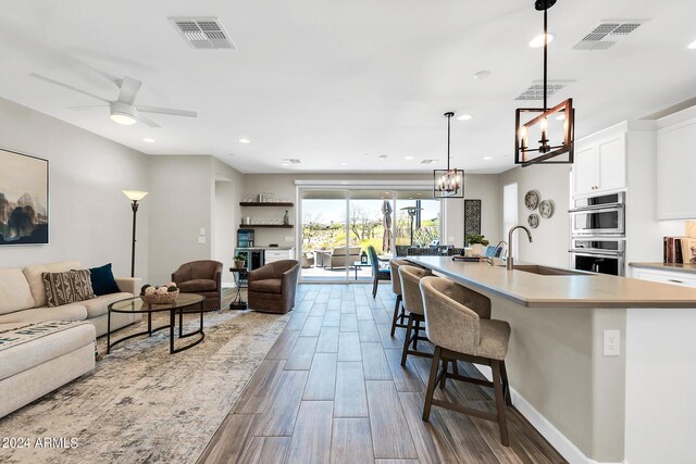 kitchen featuring ceiling fan with notable chandelier, a center island with sink, hanging light fixtures, sink, and hardwood / wood-style flooring