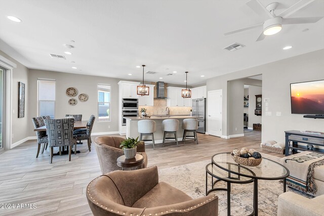 living room with ceiling fan with notable chandelier, sink, and light hardwood / wood-style floors