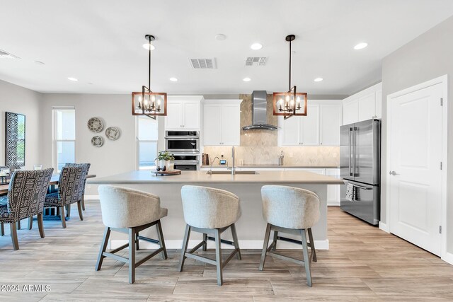 kitchen with wall chimney range hood, stainless steel appliances, a chandelier, and white cabinetry