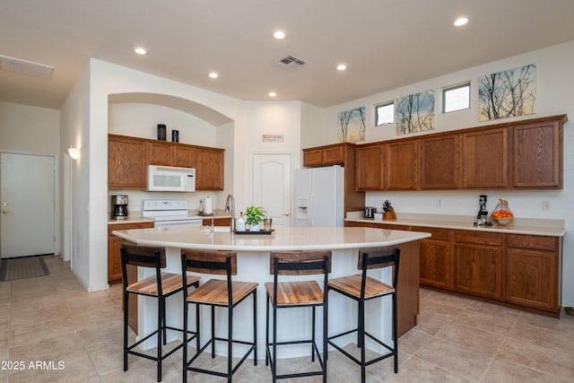 kitchen featuring a breakfast bar area, sink, an island with sink, and white appliances