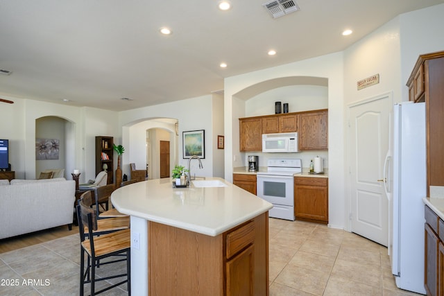 kitchen with white appliances, an island with sink, sink, a breakfast bar, and light tile patterned floors