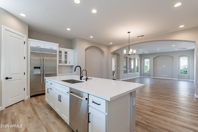 kitchen featuring white cabinets, an island with sink, stainless steel appliances, light hardwood / wood-style floors, and sink