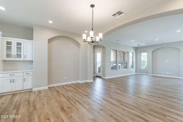 unfurnished living room with a notable chandelier and light wood-type flooring